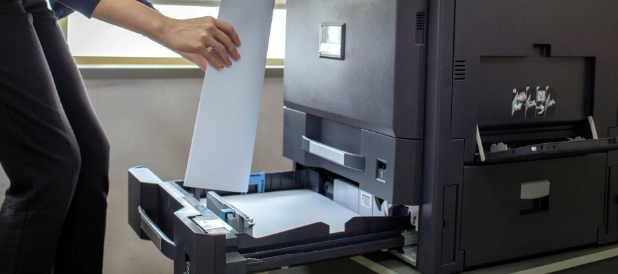 Eine Frau legt Papier in die herausgezogene, große Papierkassette eines Bürodruckers